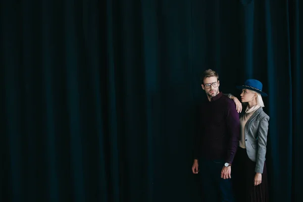 Stylish young man in glasses and blonde woman in hat near curtain — Stock Photo