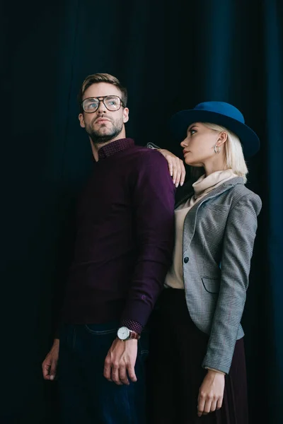 Hombre joven con estilo en gafas y mujer rubia en sombrero cerca de la cortina - foto de stock