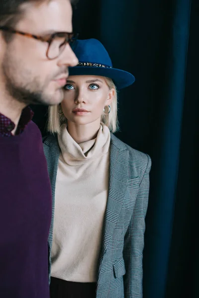 Hombre joven con estilo en gafas y mujer rubia en sombrero cerca de la cortina - foto de stock