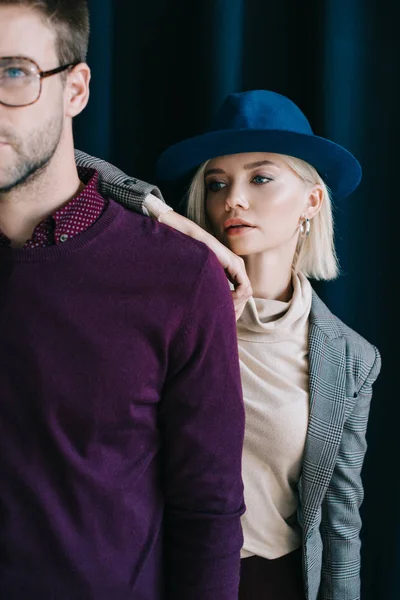 Vista recortada de hombre joven con estilo en gafas y mujer rubia en sombrero cerca de la cortina - foto de stock