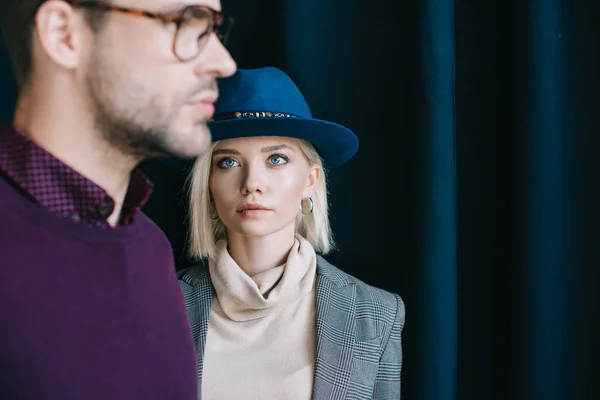 Cropped view of stylish young man in glasses and blonde woman in hat near curtain — Stock Photo