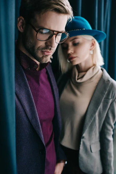 Hombre joven con estilo en gafas y mujer rubia en sombrero cerca de la cortina - foto de stock