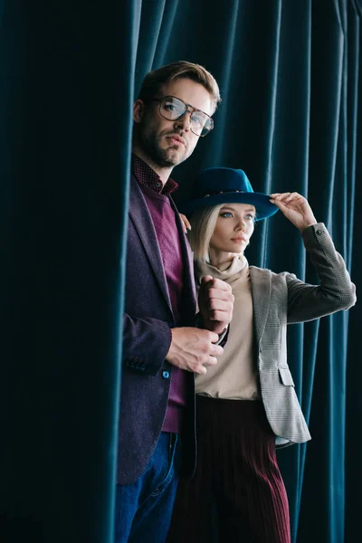 Stylish young man in glasses and blonde woman in hat near curtain — Stock Photo