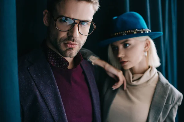 Stylish young man in glasses and blonde woman in hat near curtain — Stock Photo