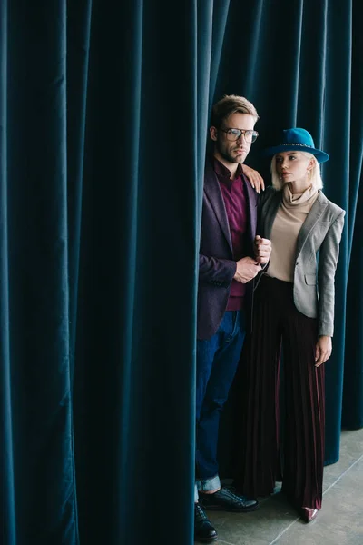 Stylish young man in glasses and blonde woman in hat near curtain — Stock Photo