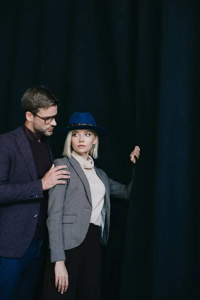 Elegante junge Frau mit Hut und Mann mit Brille in der Nähe des Vorhangs — Stockfoto