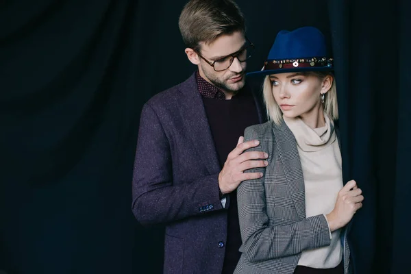 Elegant young man in glasses embracing blonde girl in hat near curtain — Stock Photo