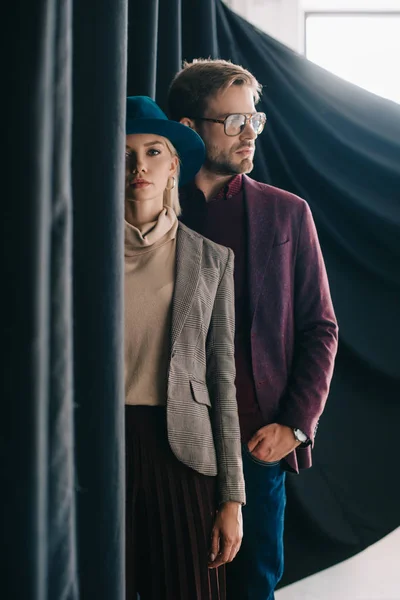 Elegante mujer joven en sombrero y hombre en gafas cerca de la cortina - foto de stock