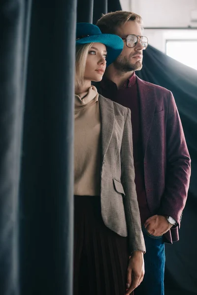 Elegante mujer joven en sombrero y hombre en gafas cerca de la cortina - foto de stock