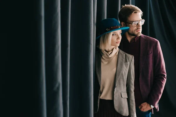 Stilvolle junge Frau und Mann, die mit der Hand in der Tasche neben Vorhang stehen — Stockfoto