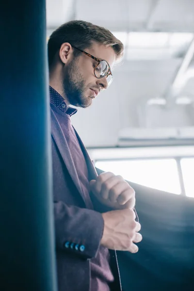 Élégant jeune homme en veste et lunettes debout près du rideau — Photo de stock