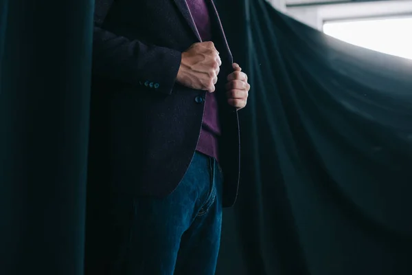 Vista cortada de jovem elegante em jaqueta de pé perto de cortina — Fotografia de Stock
