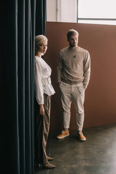 Full length view of elegant blonde woman and bearded man standing near curtain — Stock Photo