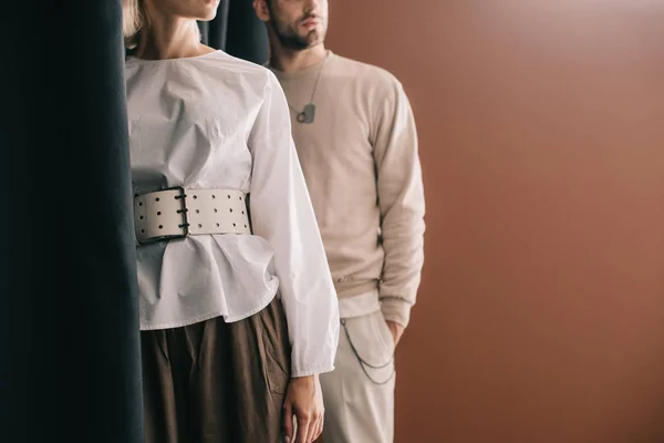 Vista cortada de elegante jovem mulher em blusa e homem de pé perto cortina em marrom — Fotografia de Stock