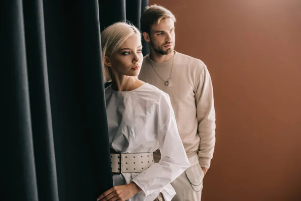 Stylische junge Frau in Bluse und Mann steht neben Vorhang auf braun — Stockfoto