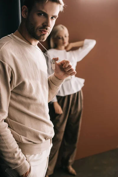 Bearded man with hand in pocket touching pendants and woman in white blouse on brown — Stock Photo