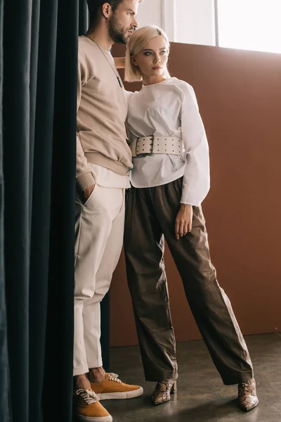 Visão comprimento total do casal elegante em pé perto de cortina no marrom — Fotografia de Stock