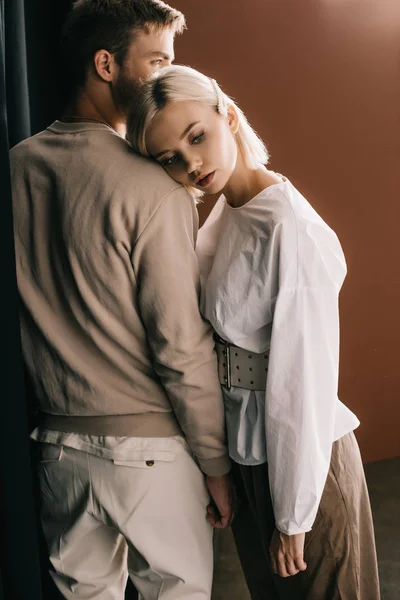 Casal elegante de pé perto de cortina e olhando para longe em marrom — Fotografia de Stock