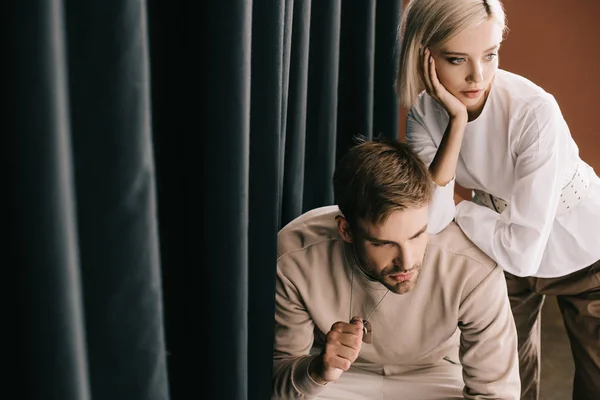 Nachdenkliches blondes Mädchen und bärtiger Mann in der Nähe von Vorhang — Stockfoto