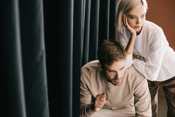 Pensive blonde girl and bearded man near curtain — Stock Photo