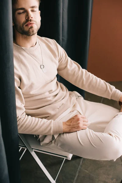 Bearded man in casual outfit sitting on chair with closed eyes near curtain — Stock Photo