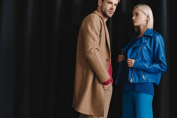 Pareja con estilo en trajes de otoño de pie cerca de la cortina - foto de stock