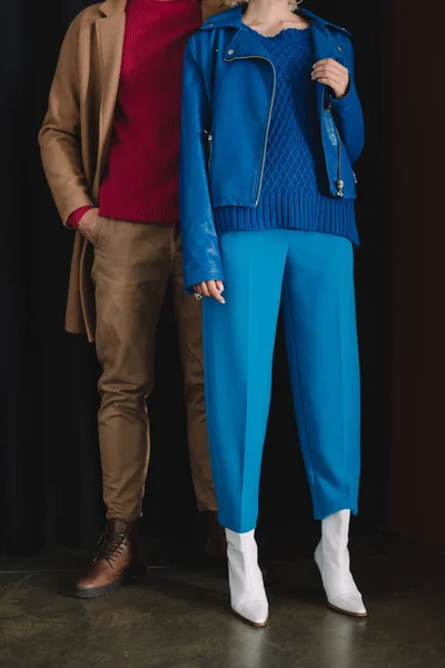 Частковий вид на стильного чоловіка в пальто і жінку в шкіряній куртці, що стоїть біля завіси — стокове фото