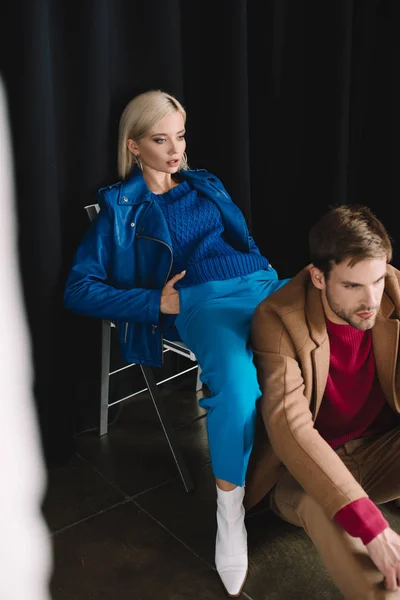 Stylisches blondes Mädchen in blauer Lederjacke sitzt auf Stuhl neben Mann im braunen Mantel — Stockfoto