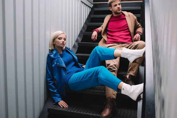 Stylish young woman and man in autumn clothes sitting on stairs — Stock Photo