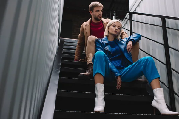 Blick von unten auf stylische junge Frau und Mann in Herbstkleidung, die auf der Treppe sitzen — Stockfoto