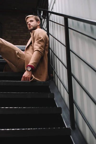 Pensive man in brown coat sitting on stairs and looking away — Stock Photo