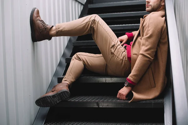 Partial view of man in brown coat and wristwatch sitting on stairs — Stock Photo