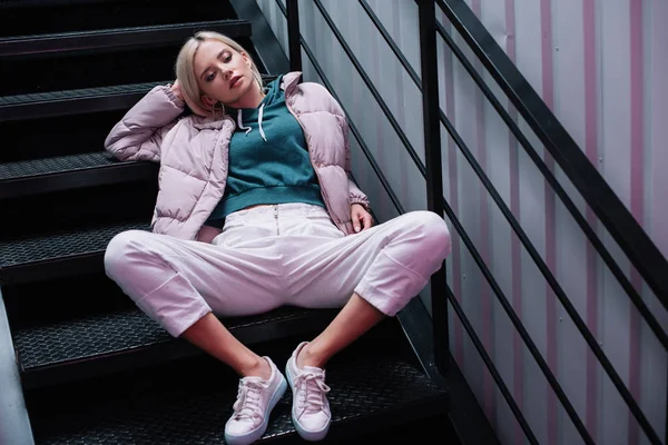 Стомлена блондинка в пуховику і кросівки, сидячи на сходах — стокове фото