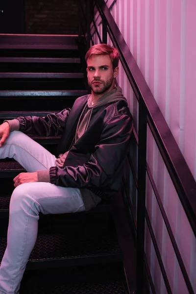 Pensive bearded young man in jacket sitting on stairs — Stock Photo