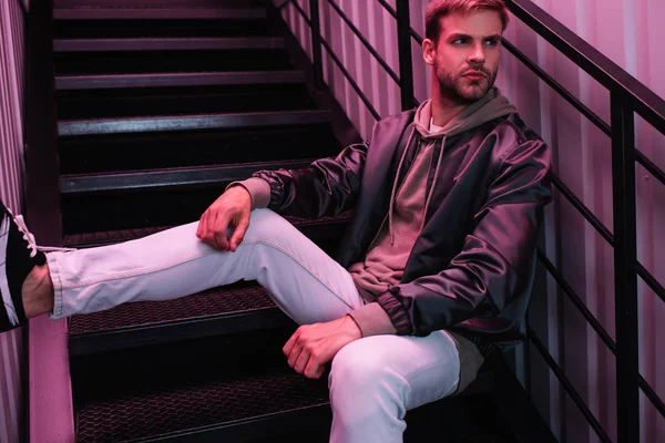 Pensive bearded young man in jacket sitting on stairs — Stock Photo