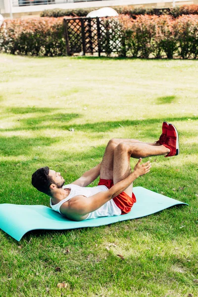 Красивый мужчина в спортивной одежде делает пресс на фитнес-коврик снаружи — стоковое фото