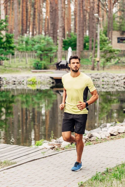 Desportista bonito correndo na passarela perto da lagoa — Fotografia de Stock