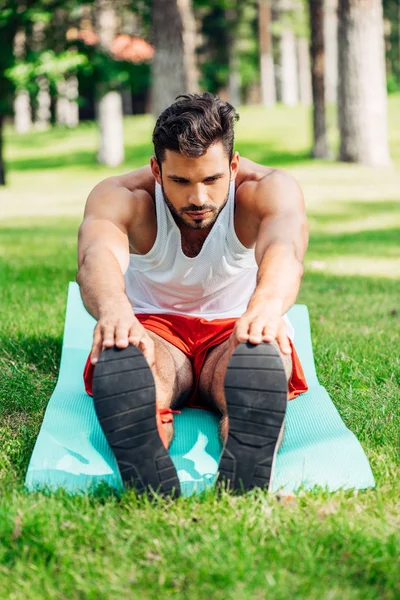 Селективное внимание привлекательного спортсмена, делающего упражнения на растяжку на коврике для фитнеса — стоковое фото
