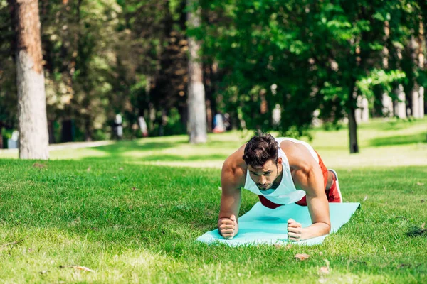 Красивый спортсмен делает упражнения на доске на коврике — стоковое фото