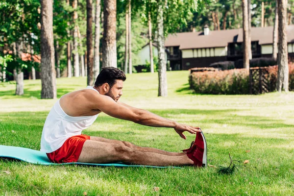 Perfil de belo desportista fazendo exercício de alongamento no tapete de fitness — Fotografia de Stock