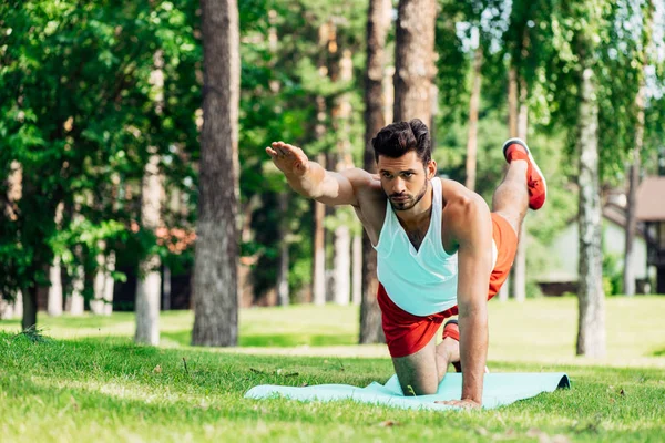 Deportista serio haciendo ejercicio en la alfombra de fitness en el parque - foto de stock