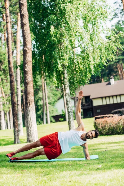 Deportista barbudo haciendo ejercicio en la alfombra de fitness y hierba - foto de stock