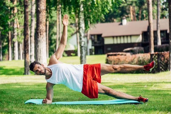 Barbudo hombre deportivo haciendo ejercicio en la alfombra de fitness y hierba - foto de stock