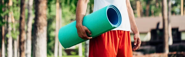 Panoramic shot of sportsman holding fitness mat in park — Stock Photo