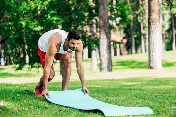Happy sportsman putting fitness mat on grass in park — Stock Photo
