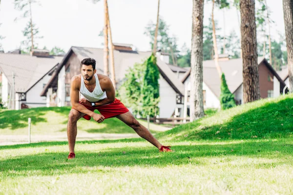 Handsome man warming up while exercising on lawn — Stock Photo