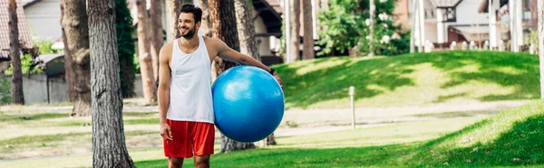 Tiro panorâmico de homem feliz segurando bola de fitness azul no parque — Fotografia de Stock