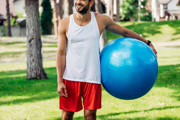 Vista ritagliata di allegro sportivo in possesso di palla da fitness blu — Foto stock