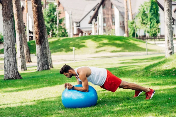 Barbudo homem no sportswear exercício no azul fitness bola no parque — Fotografia de Stock
