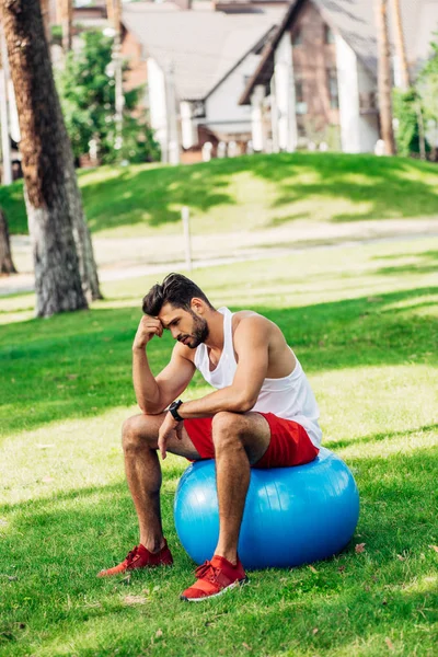Sportif bouleversé assis sur le ballon de fitness bleu dans le parc — Photo de stock